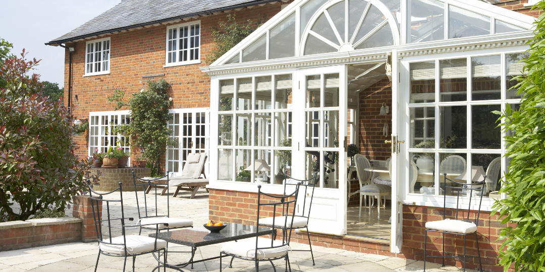 Brick home in London with elegant white conservatory style house extension and paved outdoor seating area.