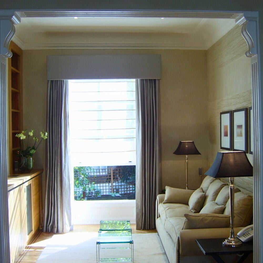Bright sitting room corner with large window, cream drapery, and a neutral palette.